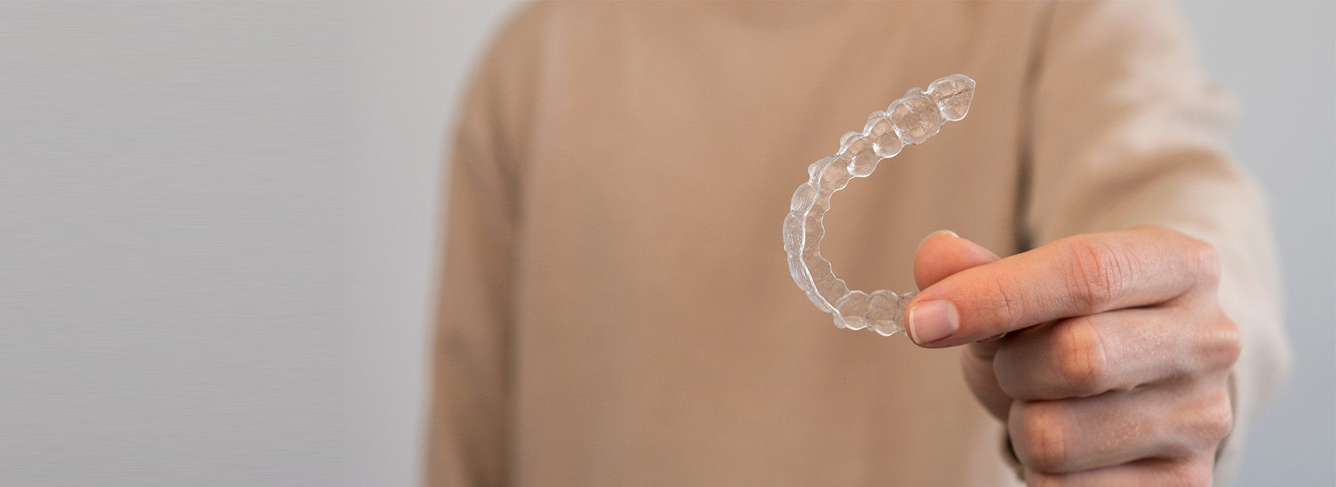 The image shows a person's hand holding a small, clear plastic bubble against a blurred background.