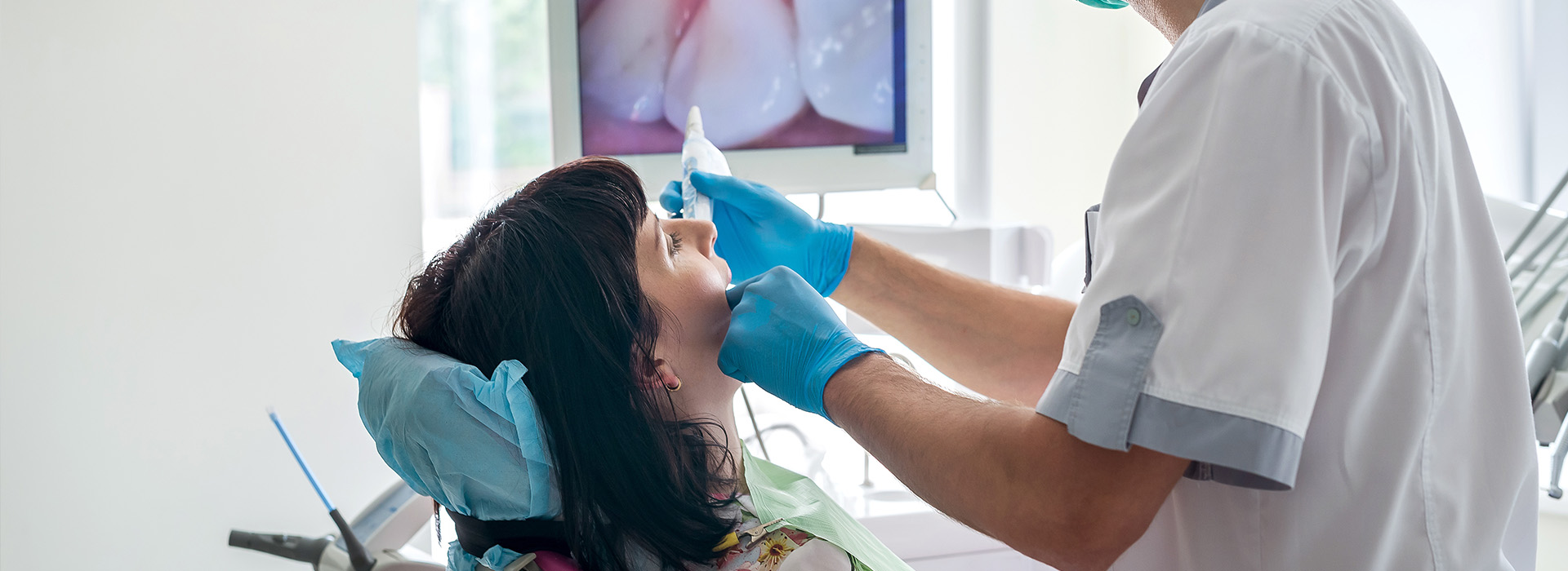 The image shows a dental setting with a person receiving dental care while a dentist works on them.
